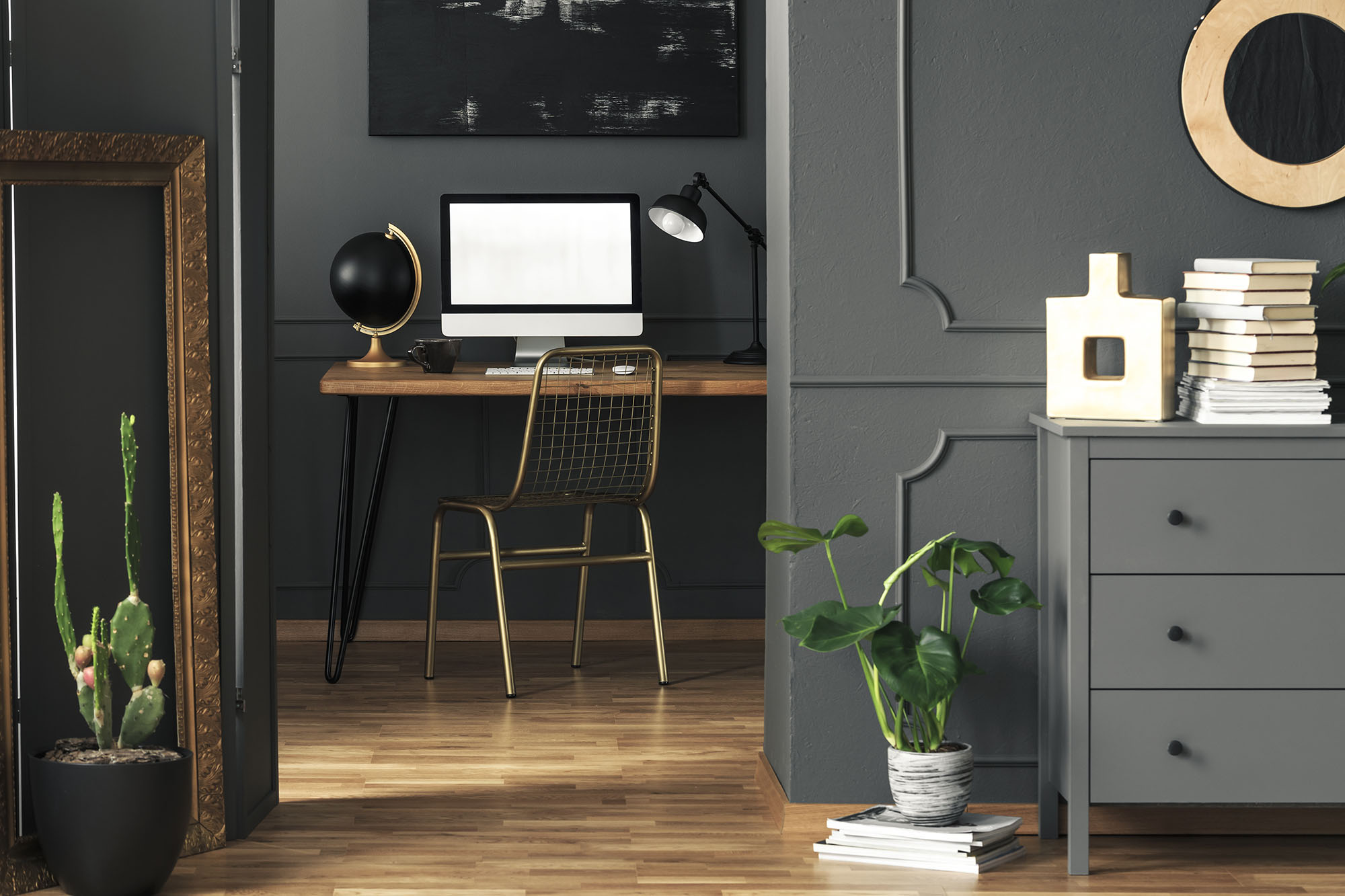 Real photo of dark living room interior with gold decor, fresh plants and wooden desk with mockup computer